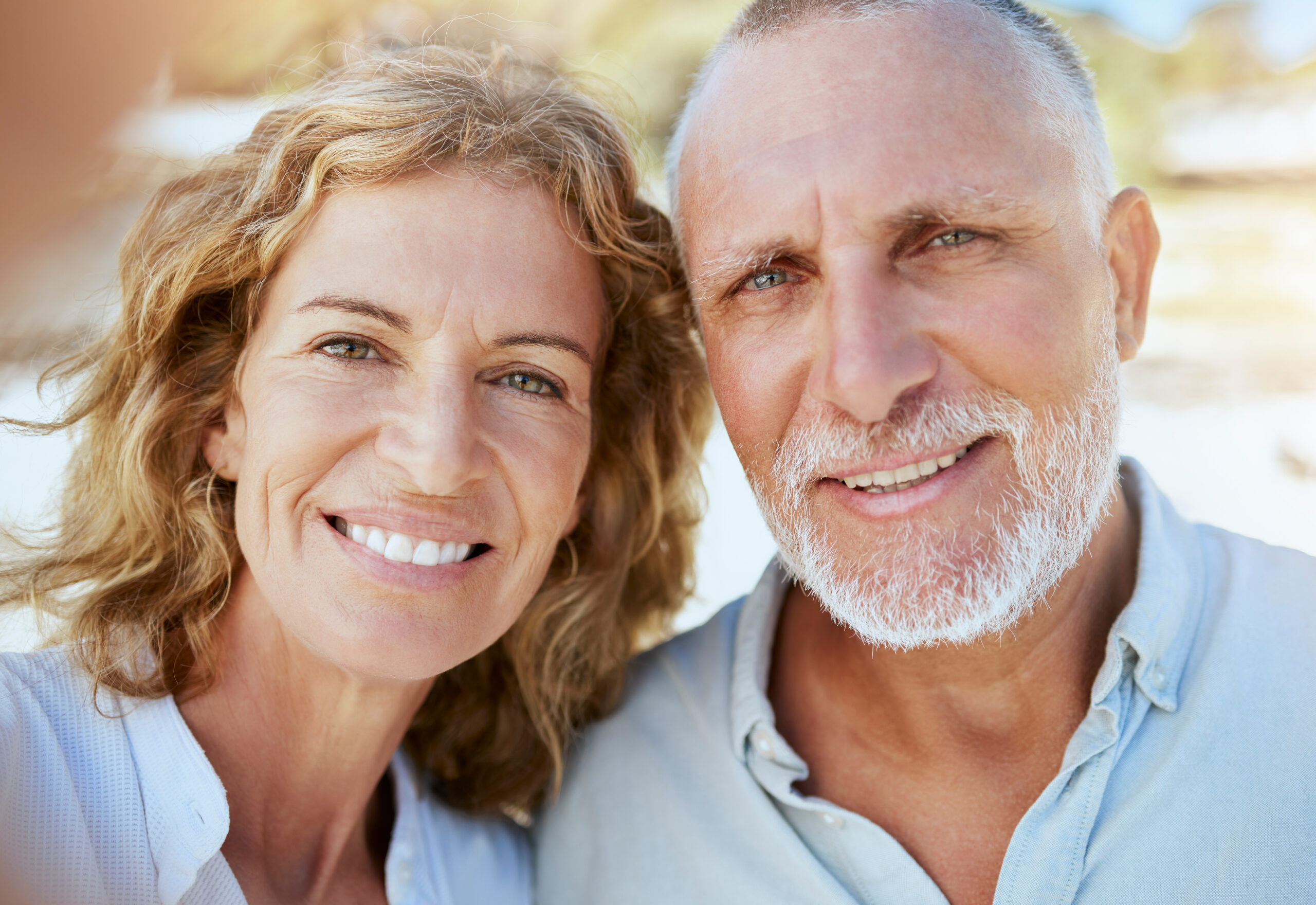 Close-up of an elderly couple smiling at the camera during a sunny outdoor selfie.